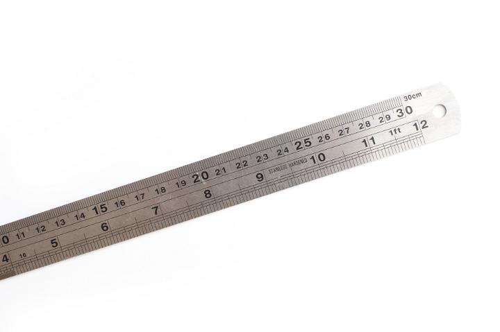 Engineering ruler with double scale marked in inches and centimetres lying diagonally on a white background with copy space