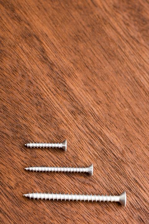 Three stainless steel wood screw sizes isolated on a timber grain background.