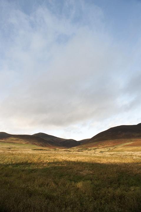 Serene scenic rural landscape with yellow field and hills at horizon, under a cloudy blue sky