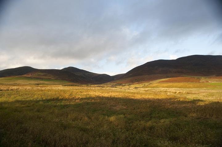 Scenic Landscape of Golden Valley Surrounded by Rolling Hills and Shrouded in Shadow from Overhead Storm Rain Clouds