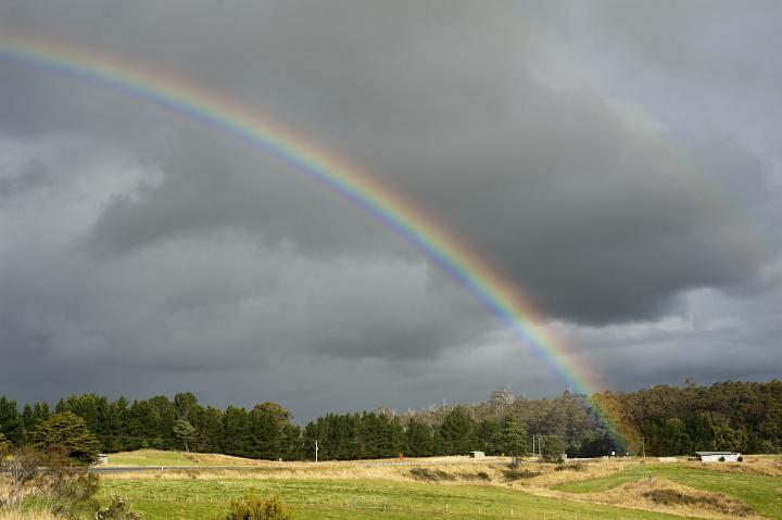 Ominous grey storm clouds with a colorful rainbow arcing gracefully over green countryside and woodland in a scenic landscape
