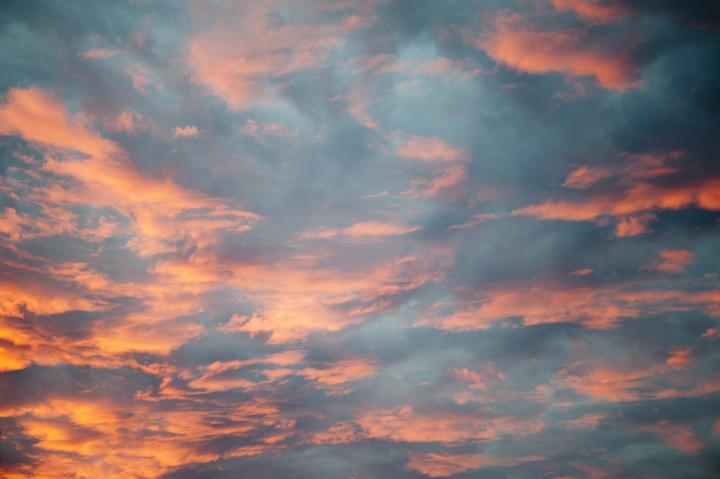 Sunset sky with pretty scattered orange tinted clouds glowing in the last rays of the sun, full frame cloudscape background