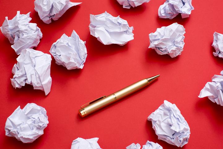 Scrapped ideas on paper, screwed into balls and isolated on a plain red background with gold pen and copy space.