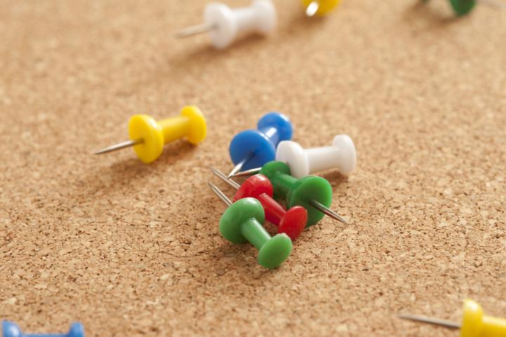 Close up Colored Unpinned Sharp Tacks on Top of Brown Cork Board
