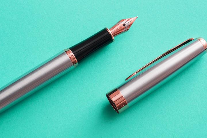 Stylish silver fountain pen and lid on a green background viewed from above suitable for use in calligraphy