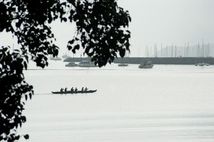 Team of six rowers in a canoe practicing for a competition on a grey overcast day in the sheltered water of a harbor