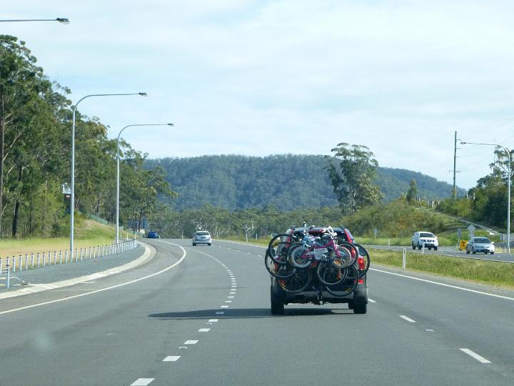 Family outing for a day of off road cycling with bicycles of all sizes strapped to a carrier on the back of a car traveling along a freeway