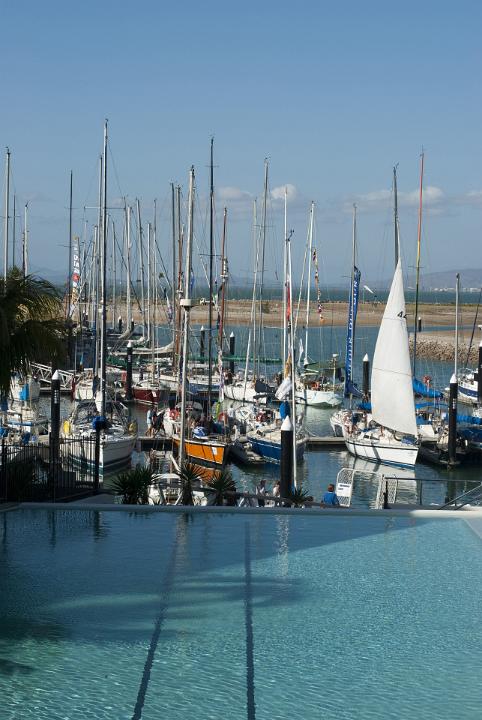 Resort marina with moored pleasure boats and yachts viewed over a sunlit swimming pool in a travel and tropical summer vacation concept
