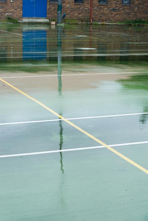 Wet green surface of an all-weather sports court with reflections of the poles and painted lines in an urban or school environment