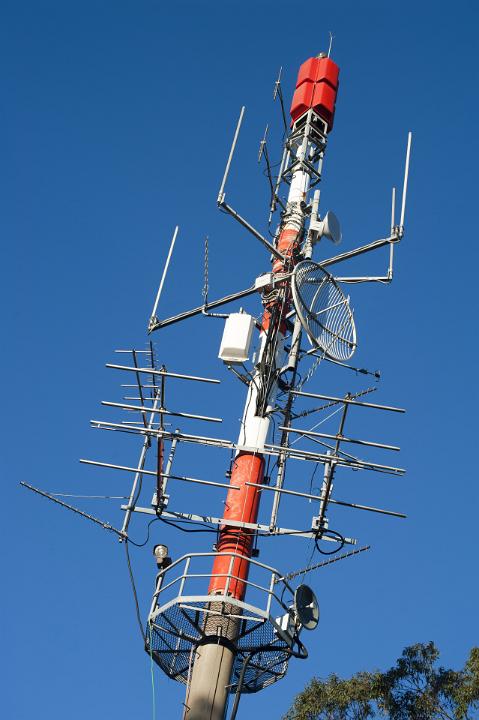 Active communication pole with transmitters, antennas and receivers for telecommunications, against a clear blue sky
