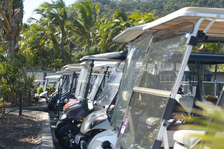 Line of golf carts parked outside a club house on a golf course with leafy green trees