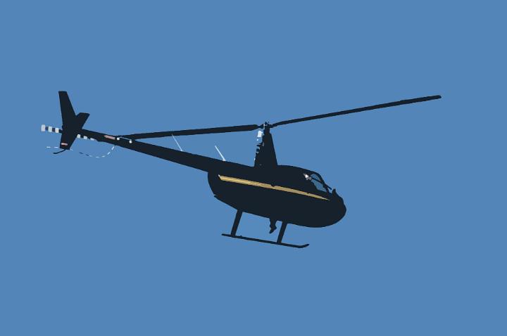 Side view of a black helicopter flying midair against a sunny clear deep blue sky