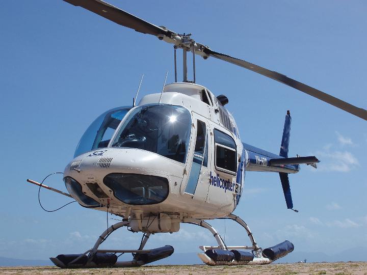 White helicopter parked on a helipad viewed at an angle from the front against a sunny blue sky