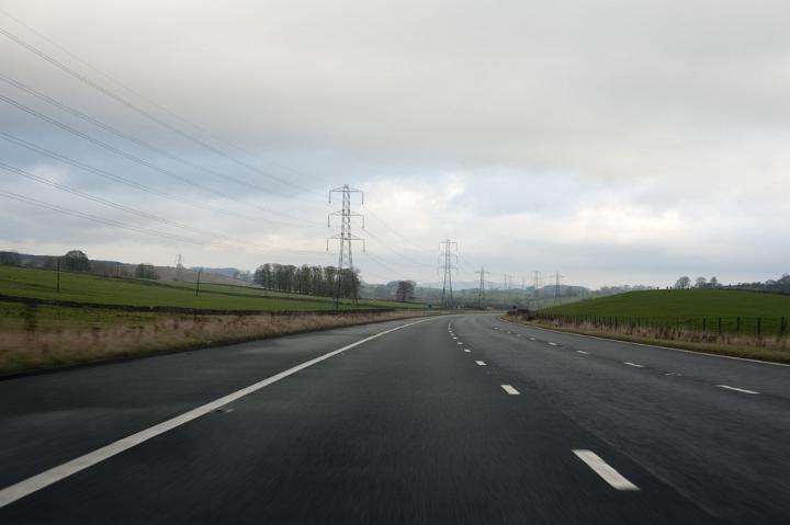 Drivers Perspective of Long Curved Highway with Transmission Towers and Power Lines Through Green Landscape and Overcast Sky