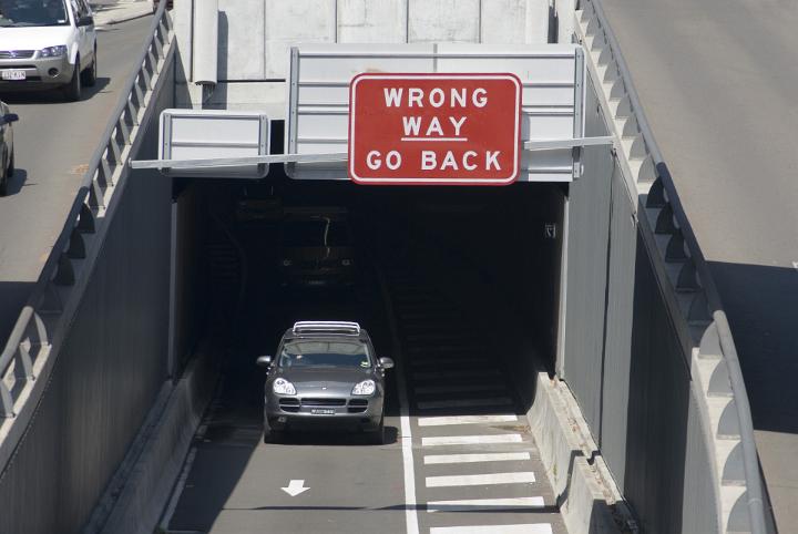 Car exiting a ramp onto the freeway under an overpass with the sign - Go Back Wrong Way