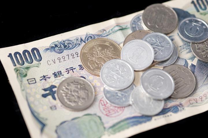 Japanese currency background with a 1000 yen banknote under assorted coins and change on a black background
