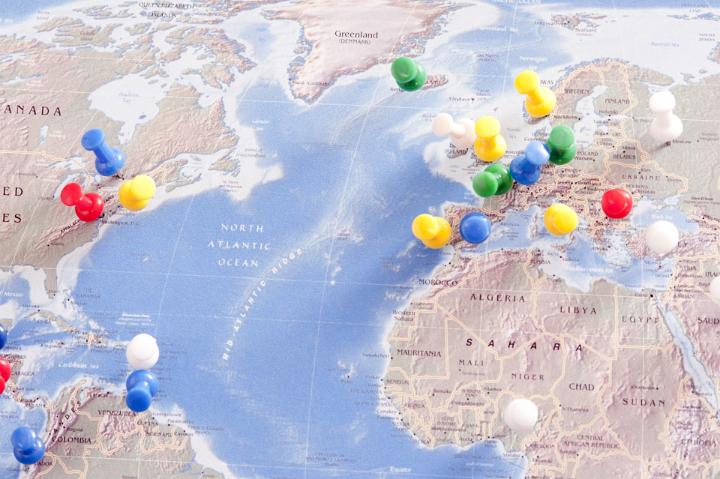 Multi-Colored Pins Tacked into Various Locations and Destinations on Flat Map of the World in Trip Planning Concept Image