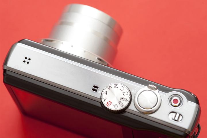Close Up View of Digital Camera Showing Dials and Buttons as seen from Above on Red Background
