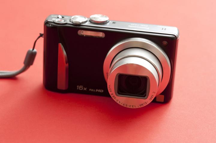 Close Up Still Life of Front View of Digital Point and Shoot Camera with Zoom Lens on Red Background