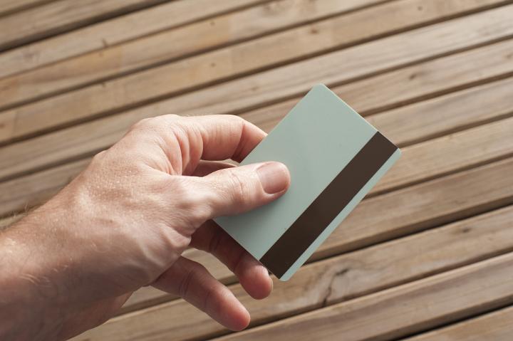 Close Up of Hand Holding Blank ATM or Credit Card with Magnetic Strip with Wooden Slat Background